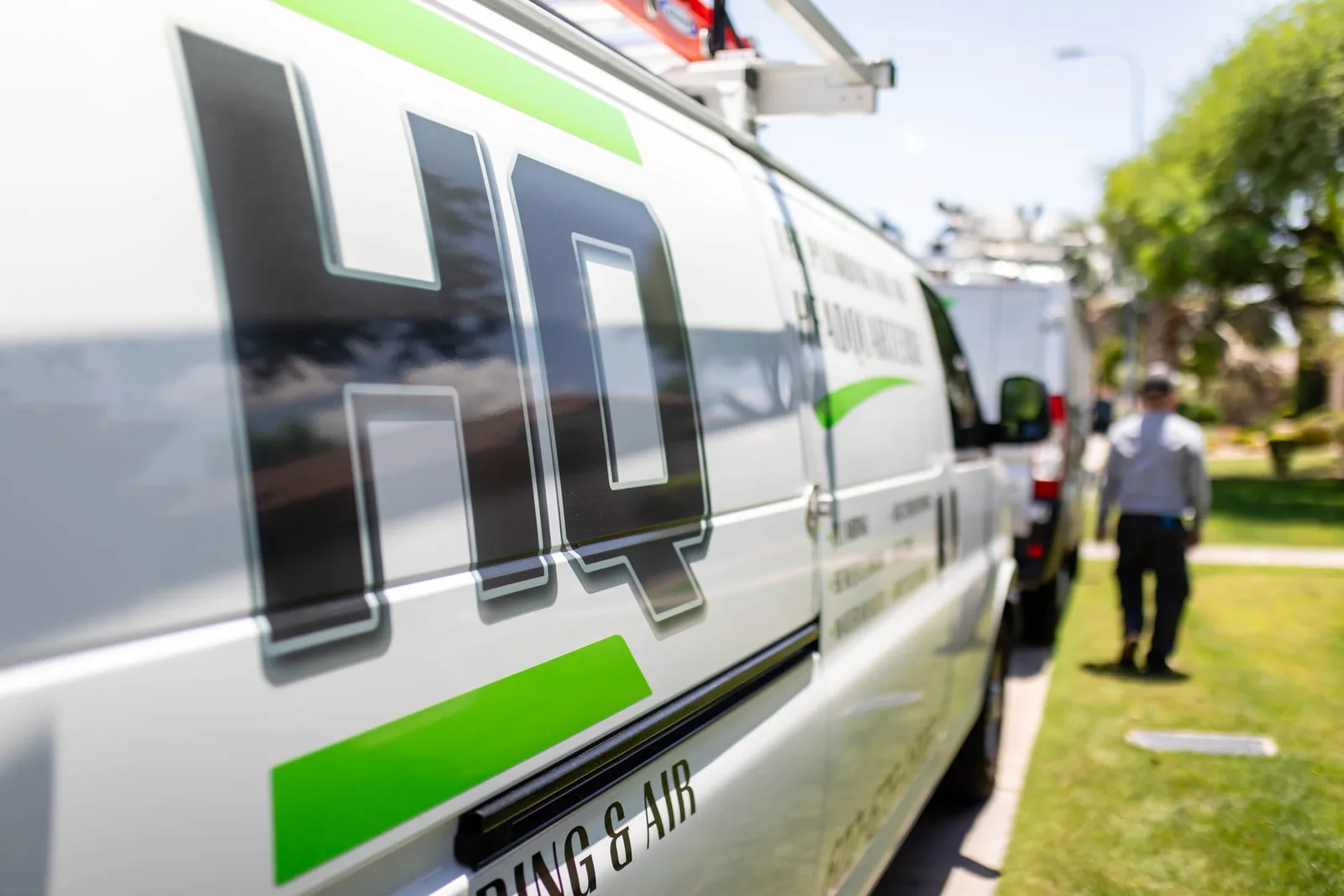 HQ Plumbing technician with branded service van in a Phoenix driveway